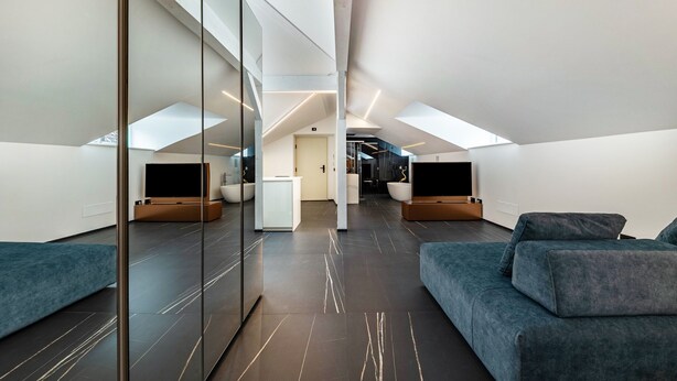 Een moderne loftkamer met een hoge nok, dakramen, een ruime modulaire bank, een flatscreen televisie en een minimalistisch design.