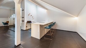 Een moderne keuken met een wit aanrecht, een donkere betegelde vloer en blauwe stoelen.