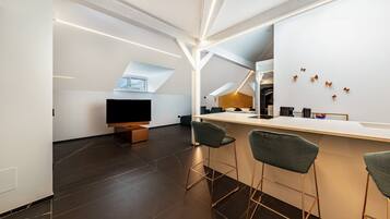 A modern kitchen with a bar area, dark flooring, and a large window.