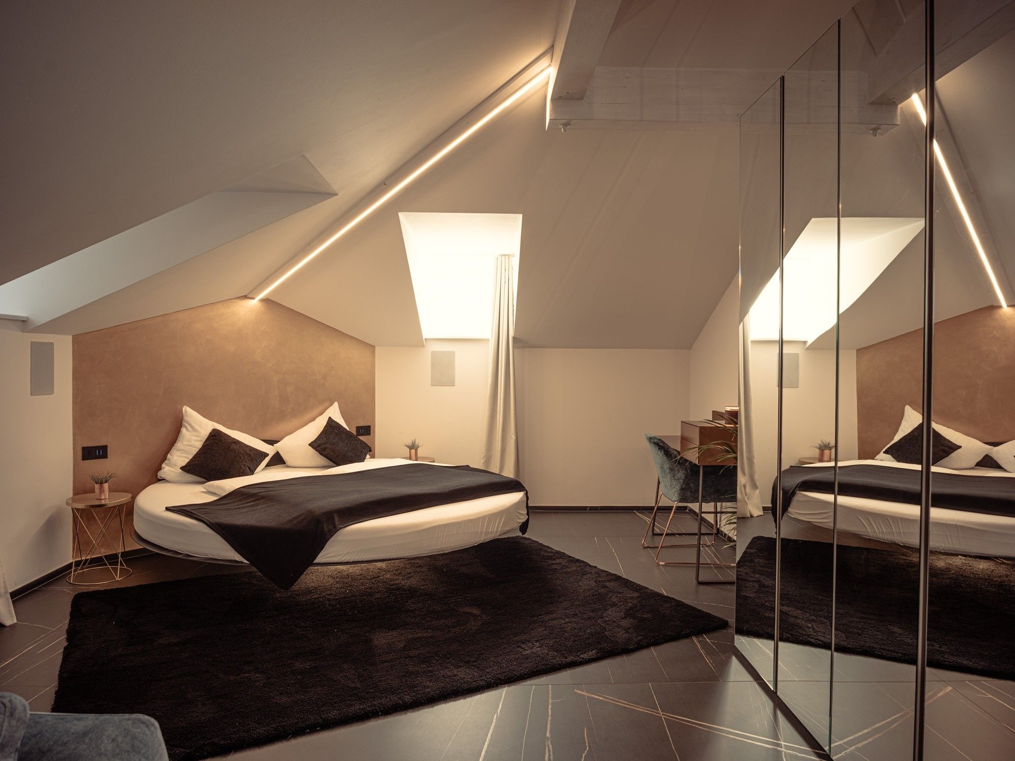 A modern bedroom with a large bed, a desk, and a mirror.