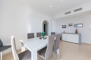 A modern dining area with a white table, grey chairs, a small cactus decoration, a white cabinet, and a framed picture on the wall.