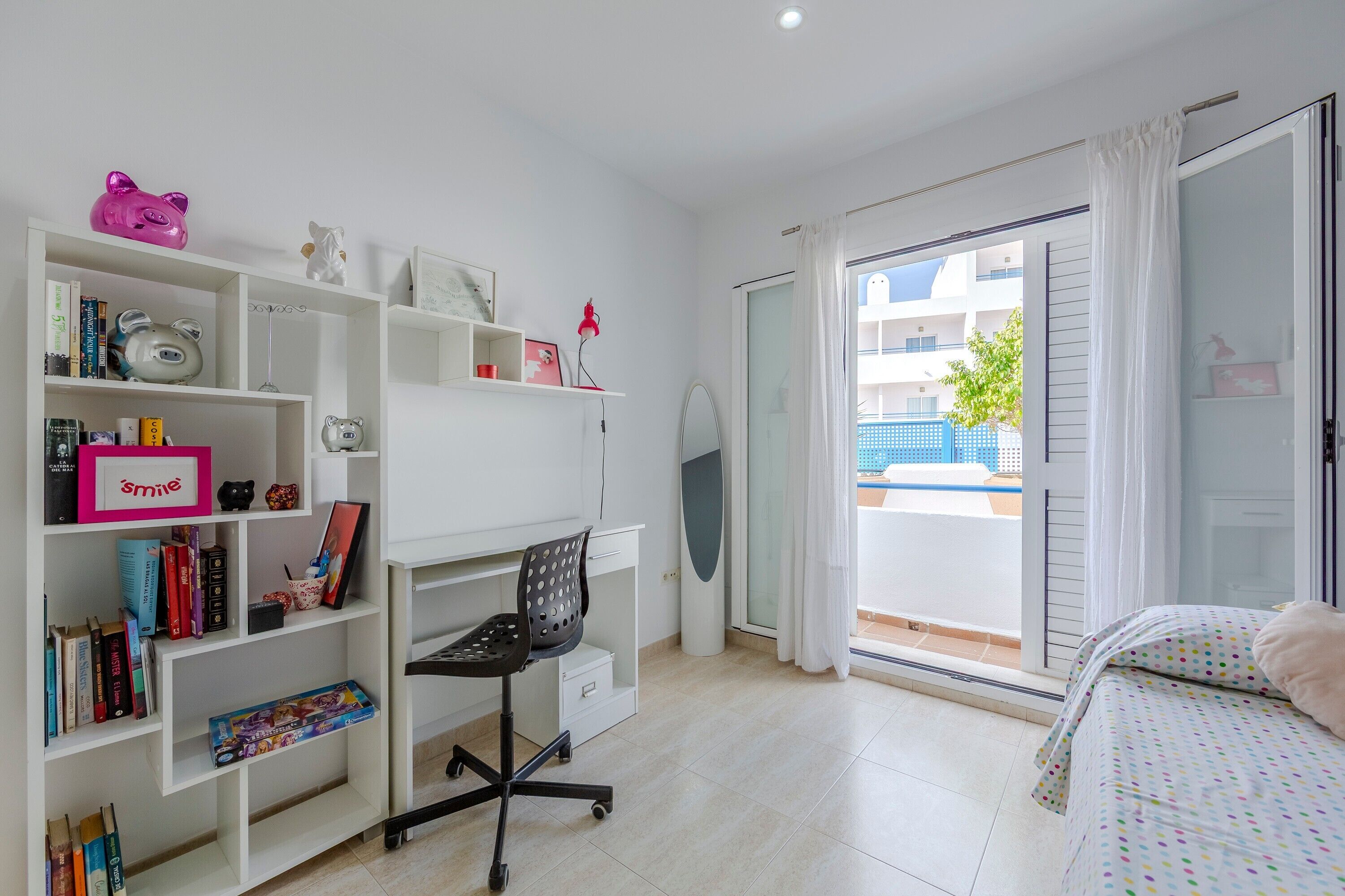 Une chambre avec un lit, un bureau avec des livres, une chaise et un balcon offrant une vue.