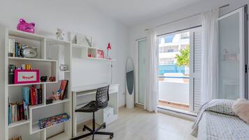 Une chambre avec un lit, un bureau avec des livres, une chaise et un balcon offrant une vue.