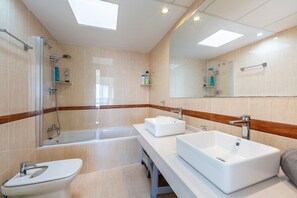 Een moderne badkamer met een douchecabine van glas, twee wastafels, een toilet en een grote spiegel.
