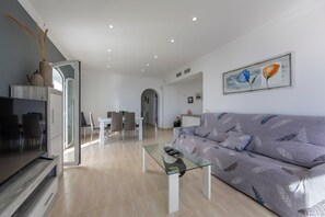 A modern living room with a glass coffee table, a sofa, and a dining area with chairs.