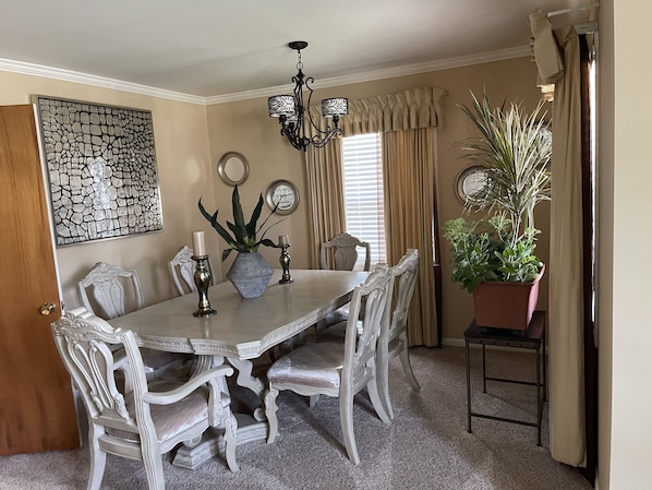 Uma sala de jantar com uma mesa grande, cadeiras elaboradas, um candelabro e arte decorativa nas paredes.