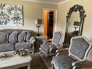 Uma sala de estar com um sofá, duas poltronas, uma mesa de centro e um espelho decorativo.