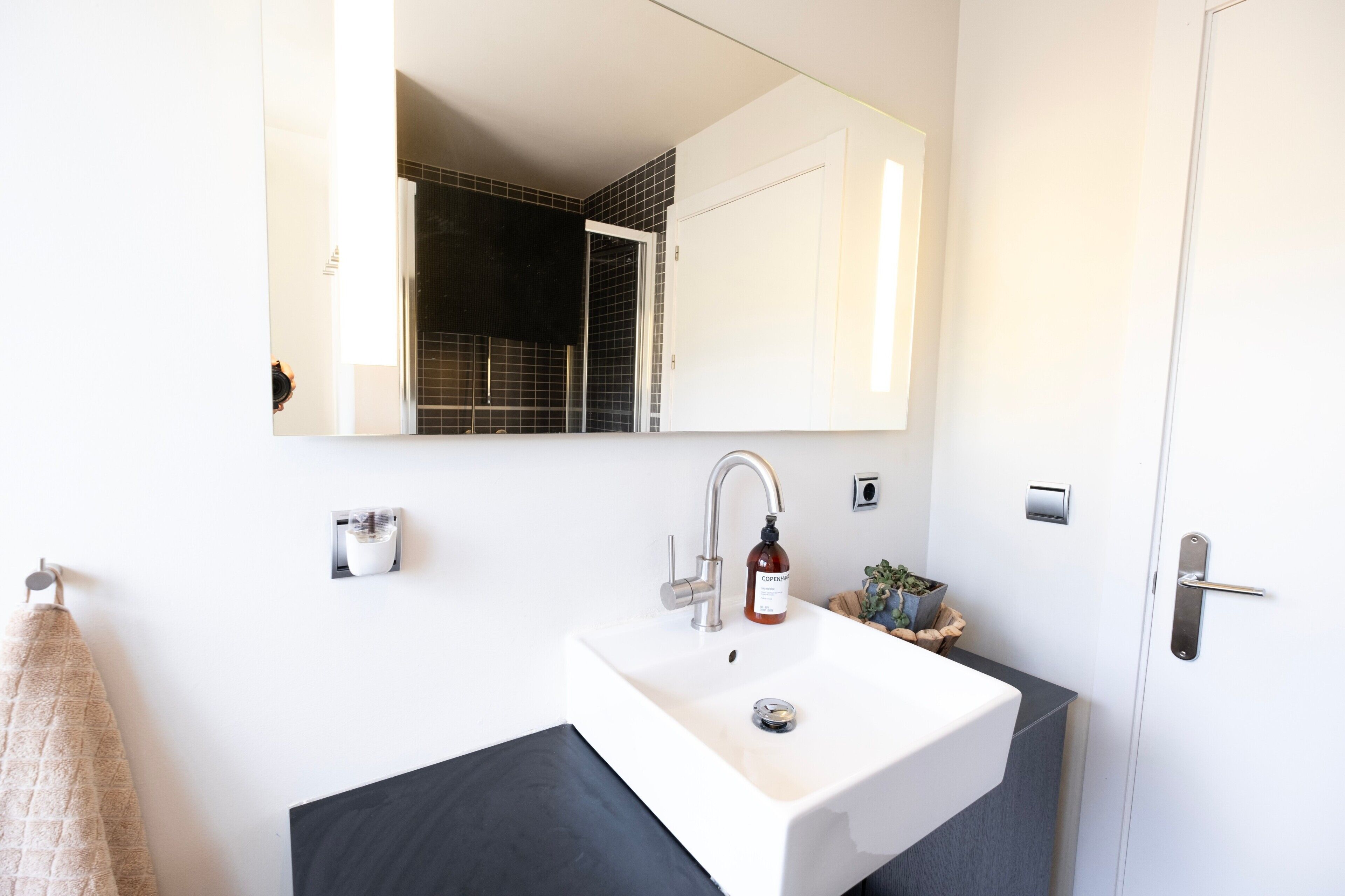 A modern bathroom with a white sink, a mirror, a towel rack, and a door.
