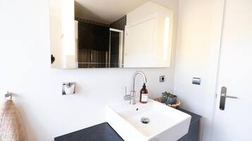A modern bathroom with a white sink, a mirror, a towel rack, and a door.