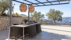 Eine Terrasse im Freien mit Tisch und Stühlen, eine Steinmauer und Blick auf die Berge.