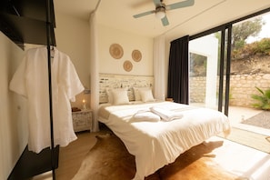 Une chambre à coucher avec un lit, un ventilateur de plafond, une table de chevet et une vue sur l’extérieur.