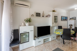 A modern living room with a flat-screen TV, white cabinetry, a dining area with a table and chairs, and a mounted air conditioner. - Beautiful Vacation Hom "Mtsrat8 "e with Air Conditioning & Terrace (Torrevieja)