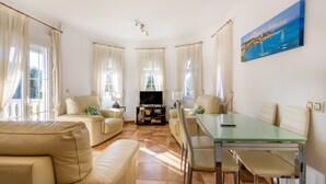 A living room with a glass table, beige sofas, and a TV.