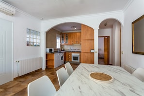 A modern kitchen with white cabinetry, a built-in oven, and a microwave. There is a dining area with a marble table and white chairs. - "5 bedroom Villa private Pool and Garden" close to the Sea with Pool & Wi-Fi (Orihuela)