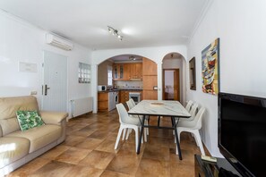 A modern living room with a sofa, dining table, and chairs, a kitchen in the background, and a TV on the right. - "5 bedroom Villa private Pool and Garden" close to the Sea with Pool & Wi-Fi (Orihuela)