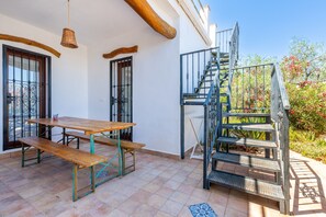 Un patio con tavolo e panche in legno, una scala in metallo e vista sul giardino.