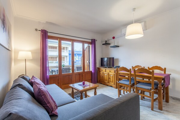 A compact living space with a sofa, a dining table with chairs, a television, and a window with curtains.