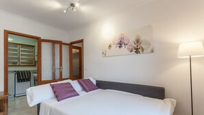 Un dormitorio con cama, mesita de noche, lámpara, un cuadro y un baño visible a través de una puerta abierta.