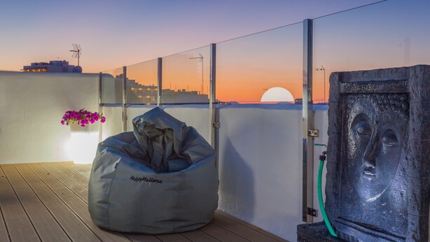 Una terraza en la azotea con un sill ón informal, una escultura de piedra y vistas al atardecer.