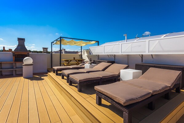 Une terrasse sur le toit, dotée de chaises longues, d’un barbecue et d’une pergola avec des parasols.