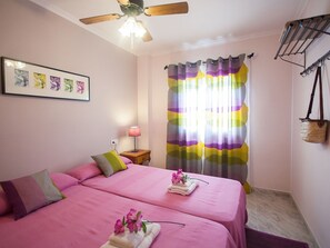 A room with two beds, a ceiling fan, a wall-mounted lamp, a curtain, and a framed picture.