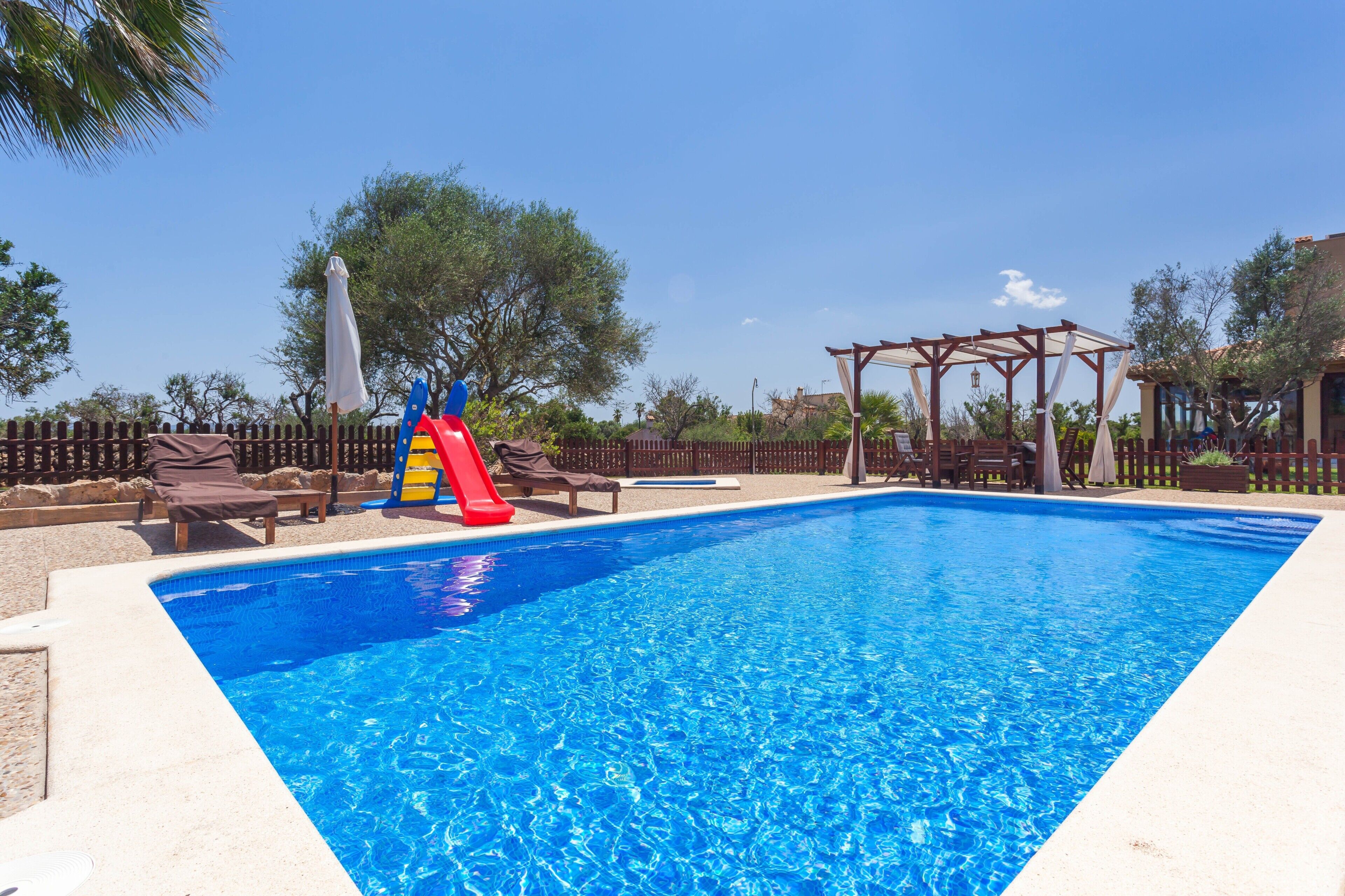 Une piscine avec un toboggan, des chaises longues et une pergola.
