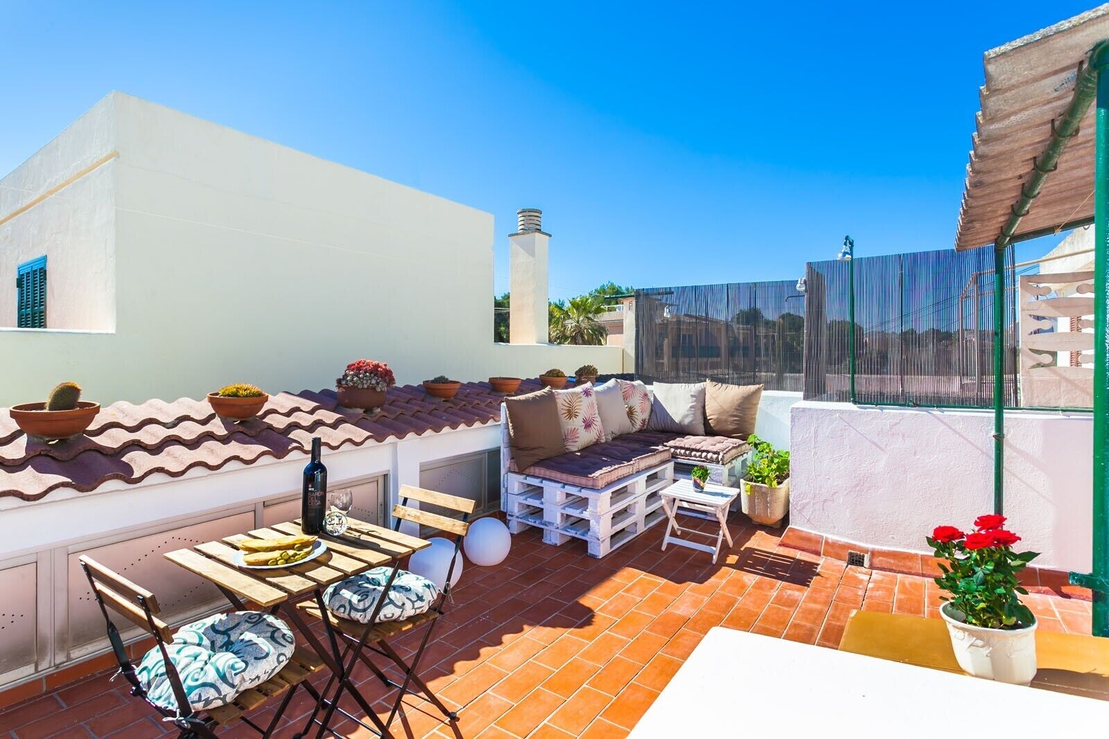A rooftop terrace with a seating area, potted plants, and a view of the cityscape.