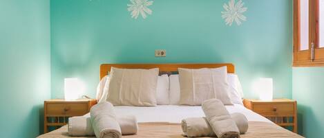 A neatly made bed with white linens and towels, a wooden headboard, and two bedside tables with lamps.