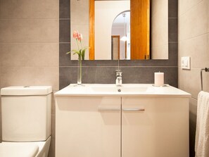 Une salle de bain avec un lavabo blanc, un miroir, des toilettes et un vase rempli de fleurs.