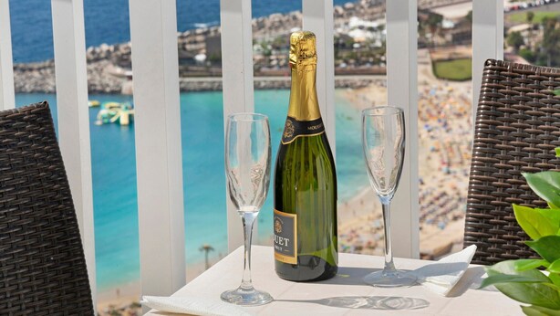 A bottle of champagne and two glasses on a table with a view of a beach and the sea.