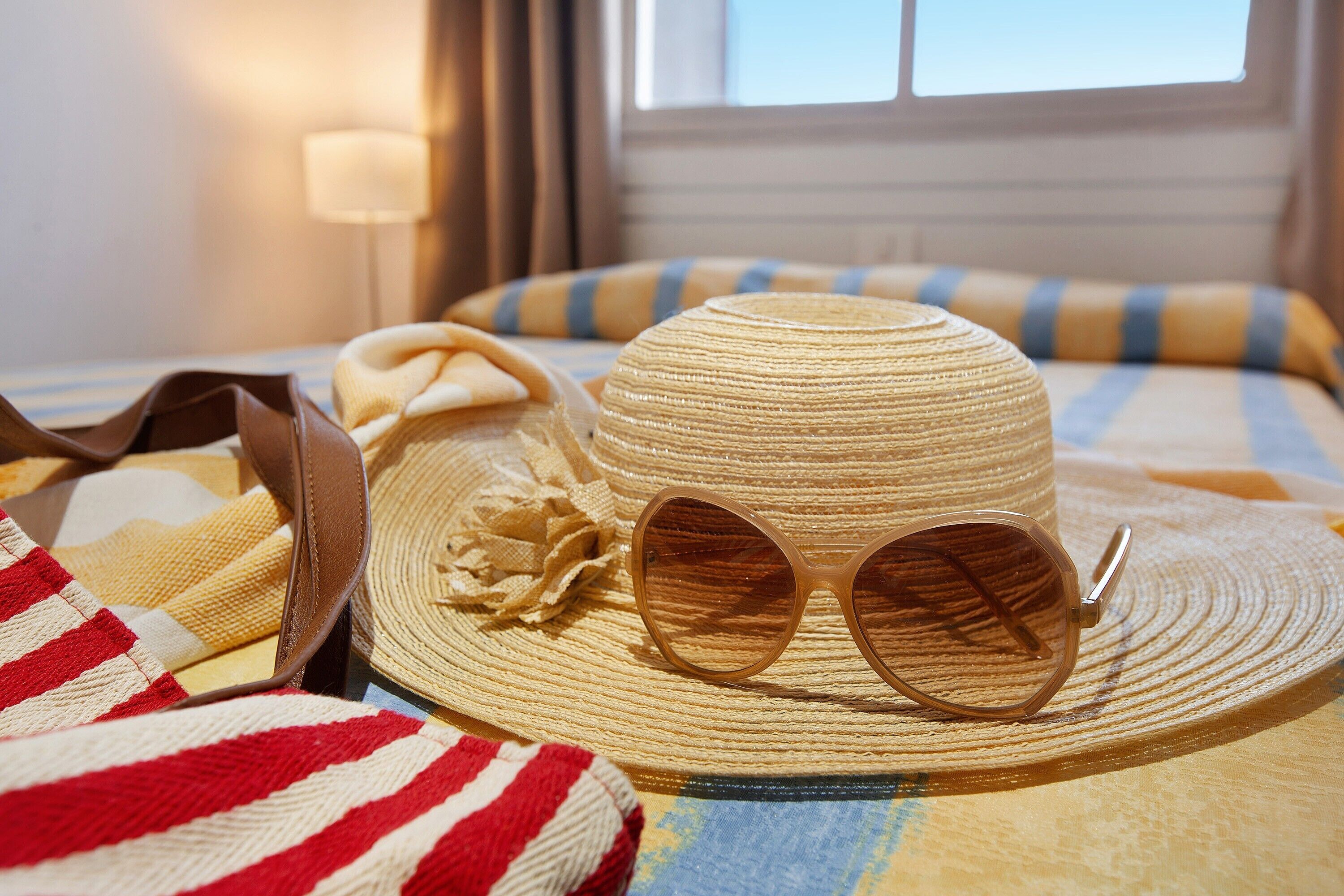 Una cama con ropa de cama a rayas, un sombrero de paja y gafas de sol encima.