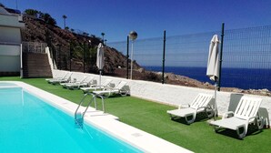 Une piscine bordée de chaises longues blanches et d’ombrelles, un escalier et une vue sur la mer.