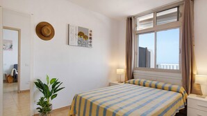 Une chambre à coucher avec un lit, des lampes de chevet, une plante en pot, un chapeau accroché au mur et une fenêtre avec des rideaux.