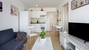 Un salon moderne avec un canapé, une table basse agrémentée d’une plante, un coin repas avec des chaises, et une cuisine en arrière-plan.