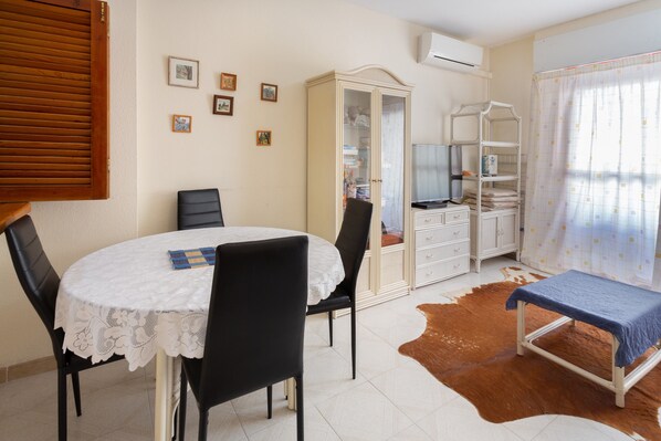 Une pièce comprenant une table ronde, des chaises, un meuble, un téléviseur et un lit avec une couverture.