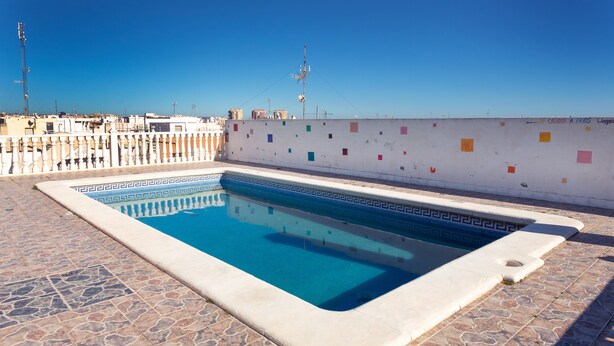A swimming pool with a geometric tile pattern, surrounded by a stone-tiled deck, and a white wall with colorful square decorations. - Beautiful Apartment "Navgts5p33-1" Near the Beach with Pool, A/C & Terrace (Torrevieja)