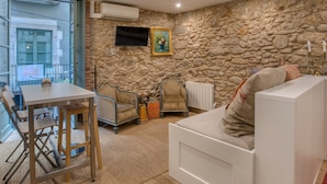 A room with a stone wall, a white sofa, a dining table with chairs, and a TV mounted on the wall. - Apartment “Old Side Girona one” with Balcony, Wi-Fi & A/C (Girona)