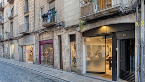A building with multiple ground-floor shops, including a visible storefront with a glass door and a sign. - Apartment “Old Side Girona one” with Balcony, Wi-Fi & A/C (Girona)