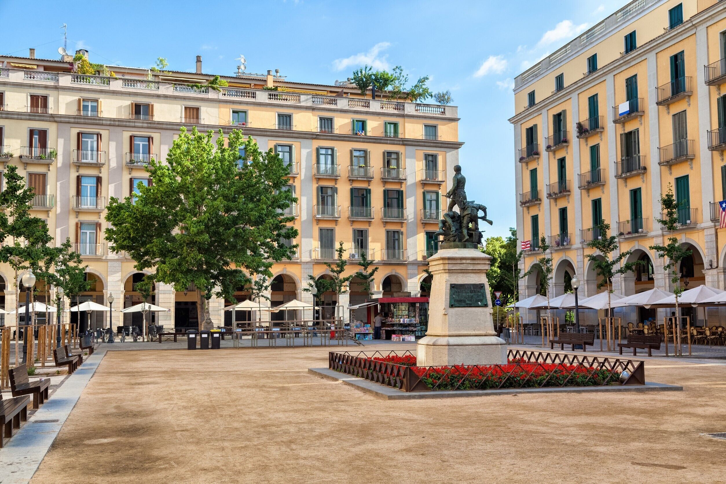 Uma praça pública com uma estátua, assentos externos e edifícios históricos.
