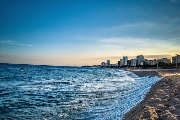 Une plage avec des vagues, une vue sur les gratte-ciel d’une ville et un ciel dégagé.