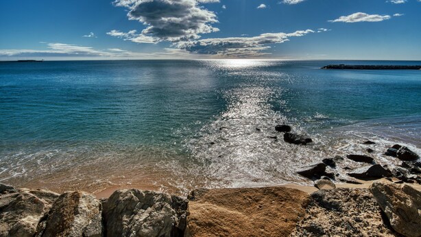 Ein Strand mit klarem Wasser, Felsen und einer entfernten Küstenlinie.