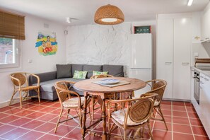 A dining area with a round table, wicker chairs, a grey sofa, and a white cabinet.