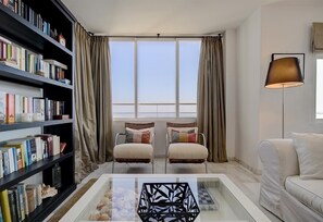 A modern living room with a large bookshelf, two armchairs, a coffee table, and a floor lamp. - Apartment "Penthouse Boulevard 401" with Pool, Terrace, Air Conditioning & Wi-Fi (Estepona)