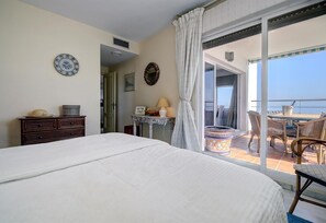 A bedroom with a large bed, a dresser, a table with a lamp, a decorative mirror, and a balcony with wicker furniture. - Apartment "Penthouse Boulevard 401" with Pool, Terrace, Air Conditioning & Wi-Fi (Estepona)