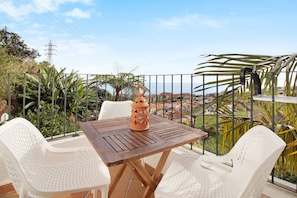 A balcony with a table and chairs, a decorative lantern, and a view of a coastal town.