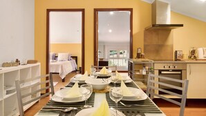 A dining area with a table set for four, a kitchen with a stove and oven, and a bedroom with a bed and nightstand. - Attic in 'Casa Amarela' with Sea & Mountain View, Wi-Fi, Garden, Parking & Garden (Caniço)