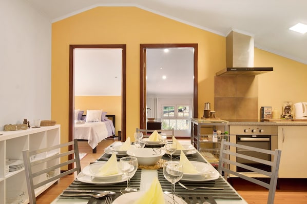 A dining area with a table set for four, a kitchen with a stove and oven, and a bedroom with a bed and nightstand.
