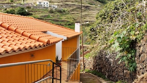 A building with a tiled roof, a stone wall, and a staircase leading to a door. - Attic in 'Casa Amarela' with Sea & Mountain View, Wi-Fi, Garden, Parking & Garden (Caniço)