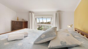 A bedroom with a bed, pillows, a dresser, a lamp, and a window with a view. - Attic in 'Casa Amarela' with Sea & Mountain View, Wi-Fi, Garden, Parking & Garden (Caniço)