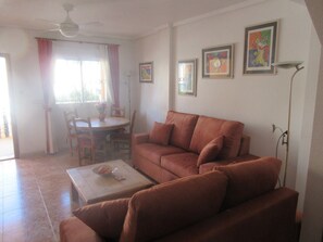 A living room with a sofa, a dining table with chairs, a coffee table, and a ceiling fan.